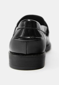 Črni brušeni usnjeni čevelj z zaobljeno zadnjo stranjo, gladko teksturo in nizkim, ravnim črnim podplatom. Šivanje po peti.