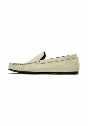 Mocassin en cuir beige avec bout moc cousu et semelle plate noire, vu de côté sur fond blanc.
