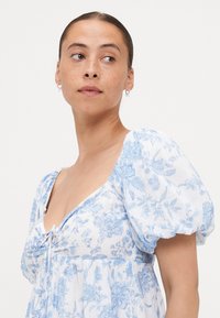 Kerge, valge lilleline kleit, millel on sinine lilleprindiga, lühikesed puffvarrukad ja V-kujuline kaelus, mille esiosas on sidumisdetail.