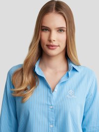 Camisa de botones azul claro con rayas verticales blancas, fabricada en un tejido suave, con cuello y bordado del logo en el lado izquierdo del pecho.