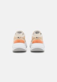 Beige sneakers med vita sulor, orange hälar, texturerat mönster och små tygdetaljer i svart, vitt och beige på baksidan.