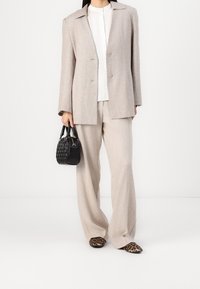 Beiger Blazer mit Reverskragen, leicht strukturiertem Blusenshirt, weit geschnittenen beigen Hosen und schwarzer geflochtener Handtasche; Ballerinas im Leopardenmuster.