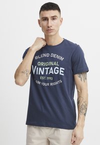 Marineblå bomullst-skjorte med et vintage grafisk trykk i hvit og grønn tekst; kortermet og med rund hals.