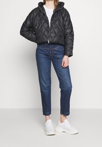 Prošívaná černá zkrácená bunda s kapucí, kombinovaná s džíny rovného střihu v modré barvě a bílými teniskami. Obsahuje přední zip a dva knoflíky.