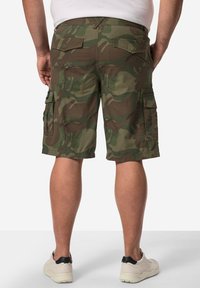Shorts cargo en camouflage de teintes vertes avec plusieurs poches, taille sécurisée et coupe décontractée. Portés avec des baskets blanches.
