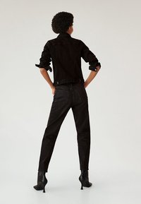 Chaqueta de mezclilla negra con mangas dobladas, combinada con jeans negros de talle alto y botines de tacón aguja, vista desde detrás.