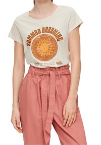 Camiseta de manga corta color crema con un gráfico de sol en naranja y marrón. Combinada con pantalones de lino rosa de tiro alto que cuentan con un cinturón atado.