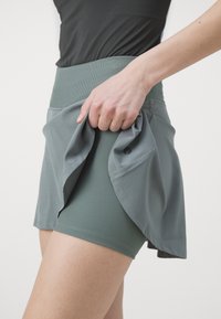 Gray athletic skirt with a pleated design, made of soft, stretchy fabric. Features a ribbed waistband and inner shorts.