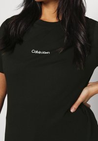 Svart bomulls t-shirt med rund hals, med en liten vit "Calvin Klein" logotyp på bröstet, mjuk struktur och avslappnad passform.