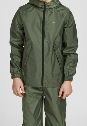 Person iført olivengrøn vandtæt hættejakke og matchende bukser med lynlås foran og elastiske manchetter på ærmerne.