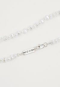 Colier din perle care prezintă perle albe de formă neregulată, accesorii din argint și un închizător cu „ICON” gravat pe un tag oval.
