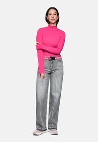 Rosa langärmliges Turtleneck-Oberteil kombiniert mit weiten grauen Jeans, die weiße Seitennaht haben, und einem schwarzen Gürtel. Die Schuhe sind hellrosa Sneakers.