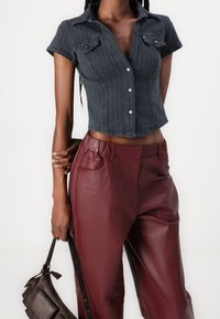 Kort gesneden donkerblauw gestreept shirt met korte mouwen, gecombineerd met bordeaux leren hooggetailleerde broek en een bruine handtas.