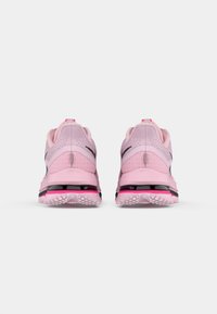 Une paire de baskets de sport rose clair vue de l'arrière, avec des accents noirs et rose fluo et des semelles texturées.