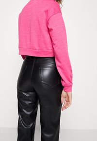 Pink cropped sweatshirt with long sleeves, paired with high-waisted black leather pants featuring back pockets and smooth texture.