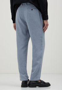 Pantalons en lin bleu clair avec une coupe décontractée, dotés de poches arrière et d'une texture lisse, associés à des mocassins noirs.