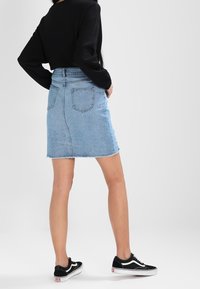 Světlá modrá džínsová sukně s třepeným lemem, vysokým pasem a zadními kapsami, spárovaná s černými teniskami a černým topem s dlouhým rukávem.