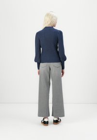 Navy ribbed sweater with puffed sleeves, paired with high-waisted gray wide-leg jeans and black and white sneakers, viewed from the back.