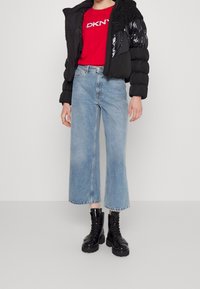 Svart puffjacka med blanka sektioner, röd t-shirt med DKNY-logga, ljusblå vida jeans och svarta snörade kängor.