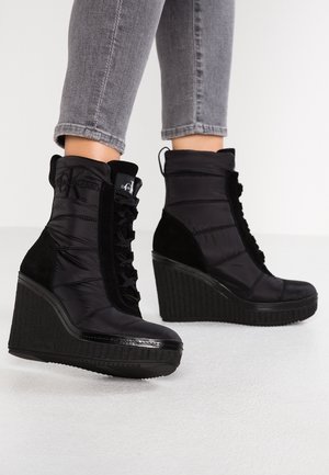 Černé klínové kotníkové boty s lesklou lakovanou špičkou, měkkým nylonovým svrškem, šněrovacím designem a texturovanou gumovou podrážkou.
