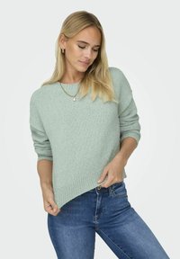 Sweater texturé vert clair avec un col rond et une coupe légèrement oversize. Présente des poignets et un ourlet côtelés. Associé à un jean en denim.
