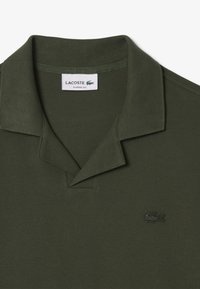 Mörk olivgrön pikétröja, klassisk passform med ribbad krage och en liten svart broderad krokodil-logotyp på vänster bröst. Strukturerad tyg.