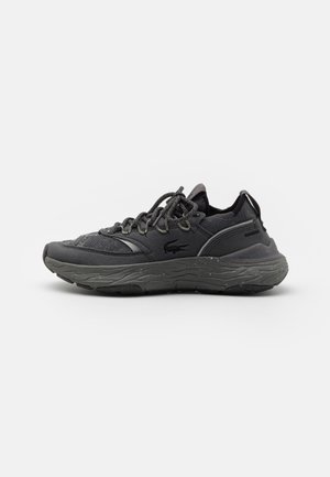 Chaussures de sport noires avec une tige en maille texturée, une semelle renforcée et une semelle intermédiaire à motif ondulé distinctif avec des accents gris.