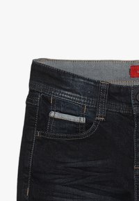 Vaqueros de mezclilla oscura con un diseño de pierna recta, que cuenta con un corte de cinco bolsillos, costuras en contraste y un forro en la parte superior de la cintura en azul claro.