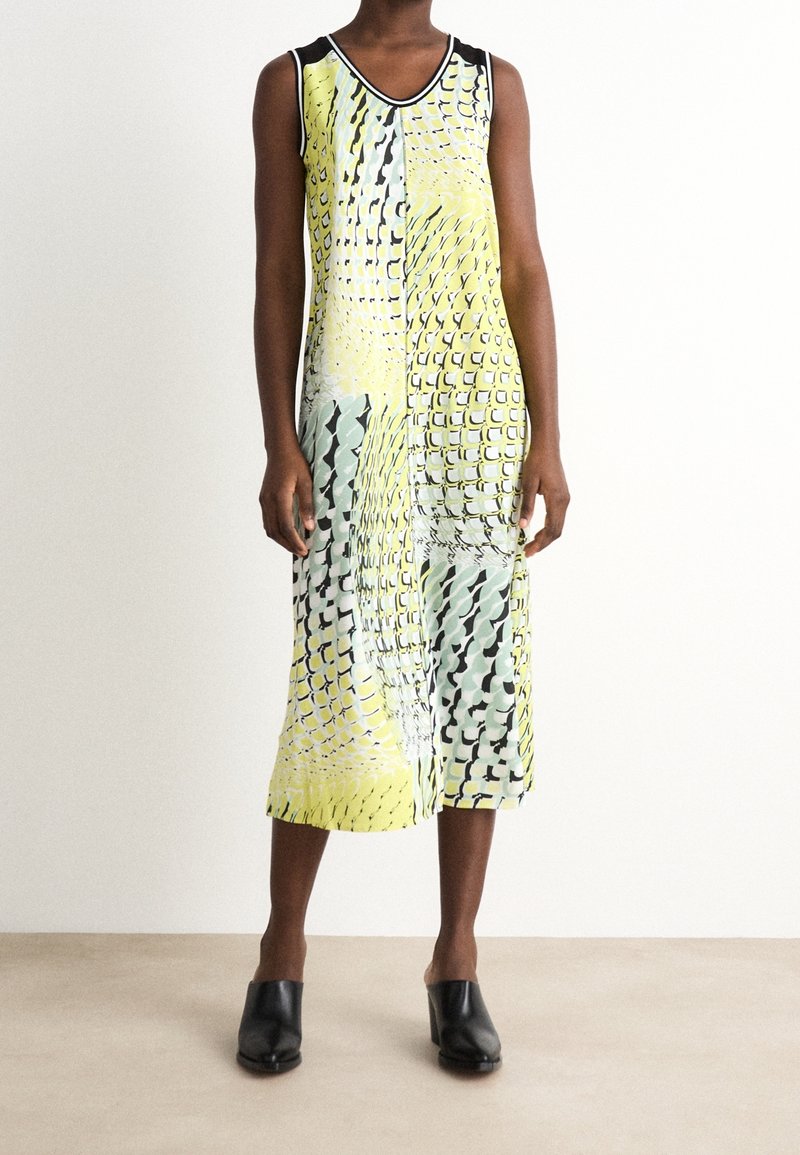 Robe sans manches aux motifs jaunes, verts et noirs ; longueur mi-mollet ; tissu lisse ; décolleté en V avec des bordures noires contrastantes.