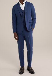 Modrý trojdílný oblek s konstrukčně tvarovaným sakem, slim fit kalhotami a bílou košilí, doplněný hnědými mokasínami. Hladká textilie.