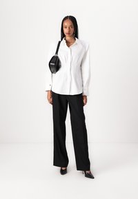 Chemise blanche à manches bouffantes, associée à un pantalon large noir. Accessoirisée d'un petit sac noir arrondi et de talons pointus.