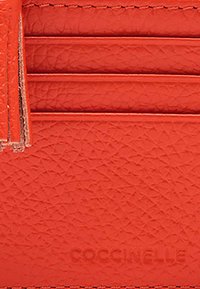Rode lederen kaartjeshouder met een gestructureerde afwerking, uitgerust met vijf kaartencompartimenten en de verhoogde merknaam "COCCINELLE" aan de voorkant.