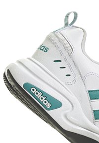 Vita sneaker med turkosa accenter, med texturerat läder, en dämpad sula och subtila perforeringar för andningsförmåga. Adidas-logotyp synlig.
