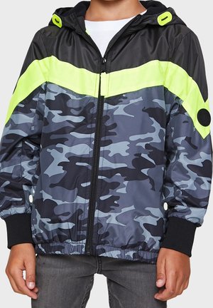 Veste camouflage en gris foncé, avec une capuche noire, une bande jaune vif, une fermeture éclair et des poignets élastiques. Tissu lisse et léger.