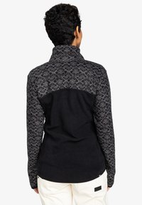 Pull en polaire avec col montant ; corps noir, épaules grises à motifs. Design texturé, tissu doux, silhouette ajustée et logo discret.