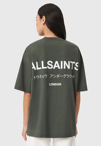 Oliivinvihreä ylikokoinen t-paita, jossa valkoiset tekstit "ALLSAINTS" ja "LONDON". Pyöreä pääntie ja lyhyet hihat, valmistettu pehmeästä puuvillasta.