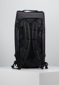 Mochila negra con correas acolchadas para los hombros, exterior liso, asa superior y herrajes laterales. Presenta una forma rectangular y un material resistente.