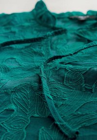 Teal lacekangas, jossa on monimutkainen lehtikuvio, kohotetut yksityiskohdat ja hieman läpikuultava rakenne. Sileä pinta ja virtaava laskos.