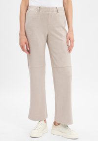 Beige, weichtexturierte Hose mit lockerer Passform, mit einem elastischen Bund und dezenten Nähten. Kombiniert mit weißen Sneakern.