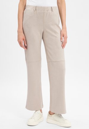 Beige, soft-textured pants with a relaxed fit, featuring an elastic waistband and subtle seams. Paired with white sneakers.