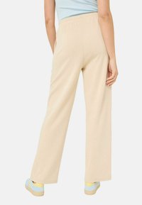 Beige wide-leg pants made of soft fabric with an elastic waistband, featuring side pockets and a smooth texture. Paired with blue shoes.