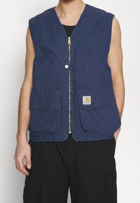 Granatowa, bezrękawnikowa kamizelka z zamkiem błyskawicznym z przodu, dwiema dużymi kieszeniami naszytymi i naszywką z logo na dolnej kieszeni. Wykonana z denimu.