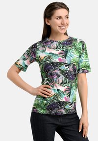 Short-sleeve t-shirt in lightweight fabric featuring a vibrant tropical leaf print in green, purple, and blue against a light background.