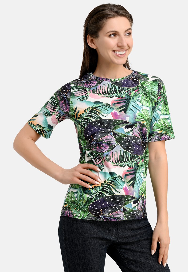 Short-sleeve t-shirt in lightweight fabric featuring a vibrant tropical leaf print in green, purple, and blue against a light background.