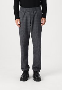 Pantalons à carreaux gris avec une taille élastique, présentant une coupe décontractée et une texture lisse, associés à des chaussures noires à lacets.