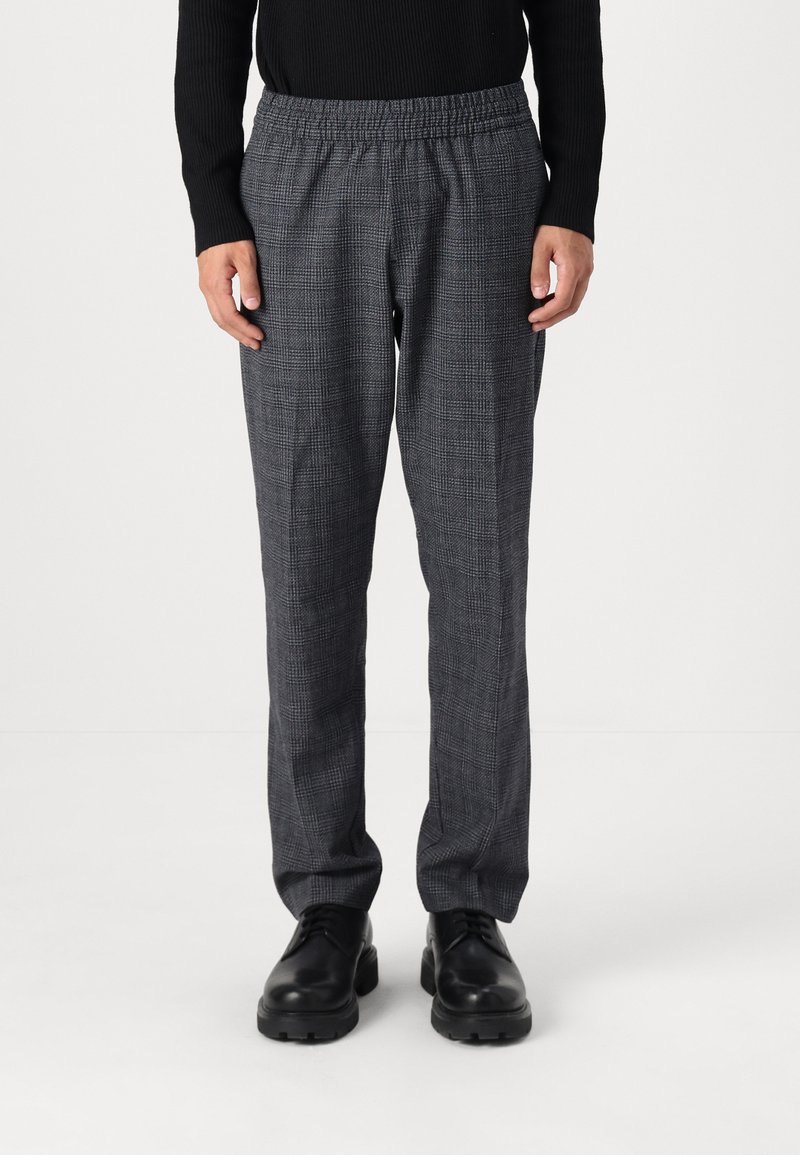 Pantalons à carreaux gris avec une taille élastique, présentant une coupe décontractée et une texture lisse, associés à des chaussures noires à lacets.