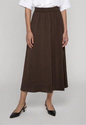 Femme portant une jupe midi marron avec une ceinture élastique, associée à des talons slingback noirs à bout pointu et une chemise blanche à manches courtes.