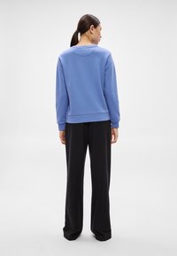 Felpa blu con scollo rotondo, polsini e orlo a costine, abbinata a pantaloni neri a righe sottili. Texture liscia, taglio aderente.