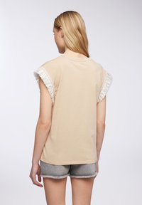 T-shirt in cotone beige con bordo in pizzo bianco arricciato ai lati delle maniche, vestibilità comoda, scollatura rotonda, abbinato a pantaloni corti in denim grigi.
