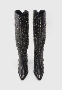 Botas negras hasta la rodilla con puntas metálicas afiladas y varios studs metálicos y adornos en patrones geométricos.